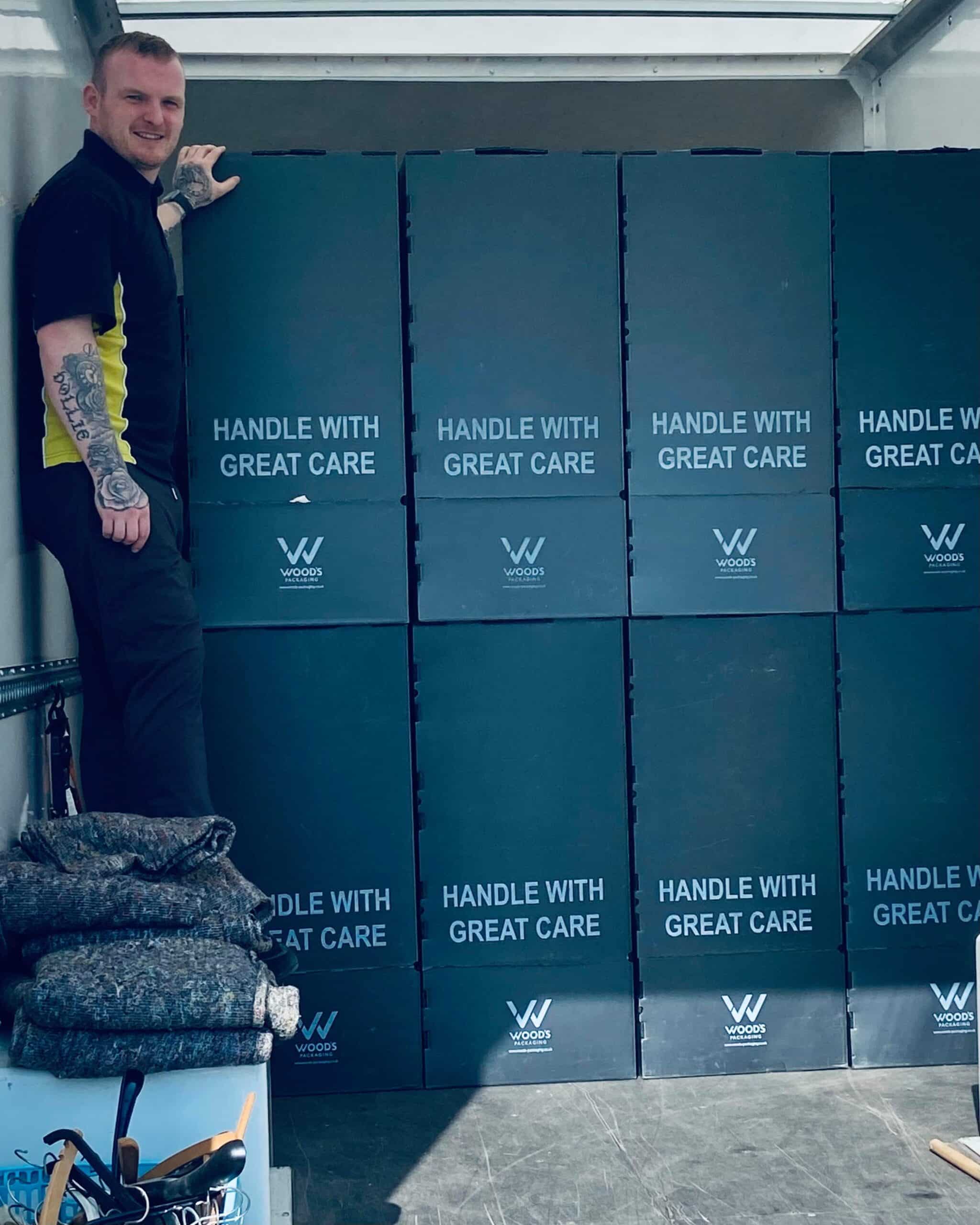 Craig Atkinson Removals team member standing beside stacked wardrobe boxes labelled ‘Handle with Great Care’ inside a removals van.