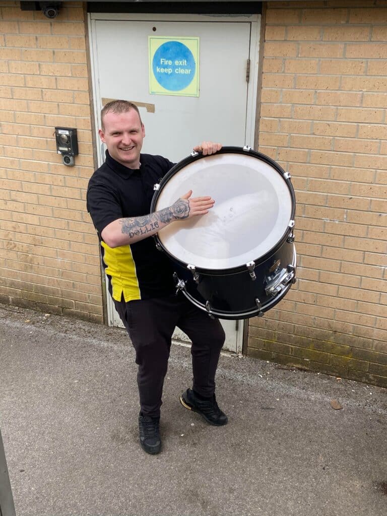Craig Atkinson smiling and holding a drum outside the company’s premises, showing the friendly and down-to-earth team spirit behind Craig Atkinson Removals.