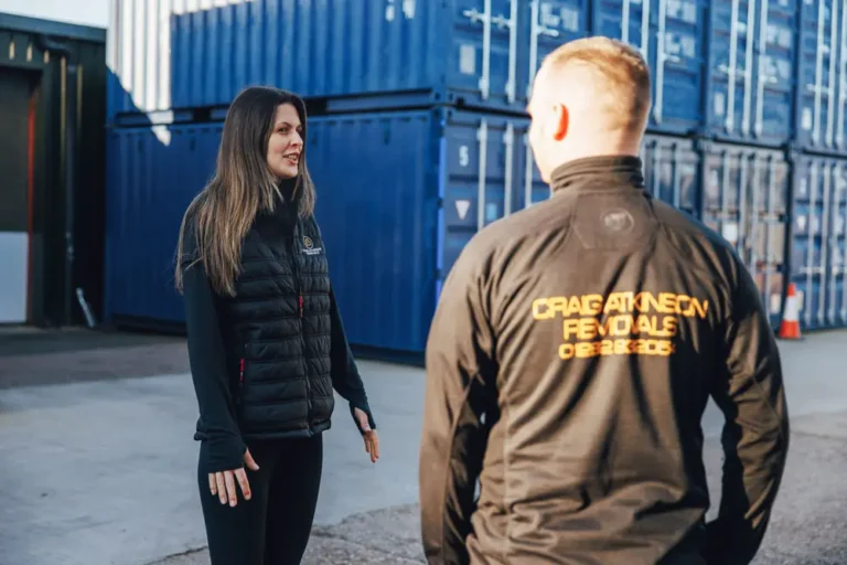Two members of Craig Atkinson Removals talking at a storage yard, wearing branded uniforms.