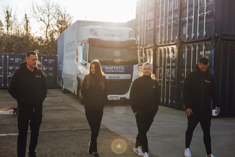 Craig Atkinson Removals and Warren’s Removals teams walking in front of storage containers and removal truck.