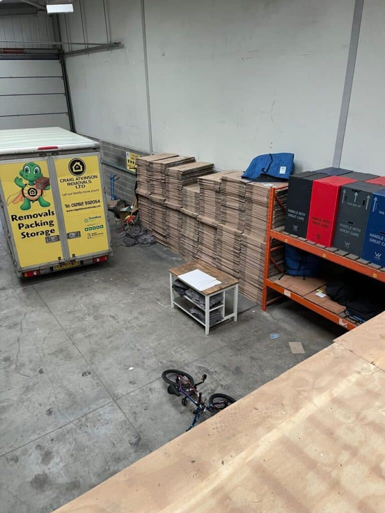 Interior of Craig Atkinson Removals warehouse with boxes stacked high, storage shelves, and branded removals van.