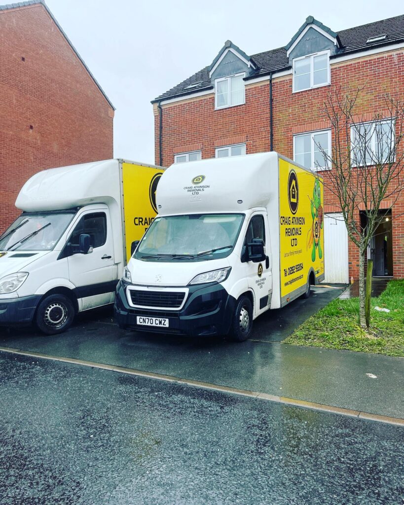 Craig Atkinson Removals vans parked outside a modern red-brick townhouse in Manchester during a local move.
