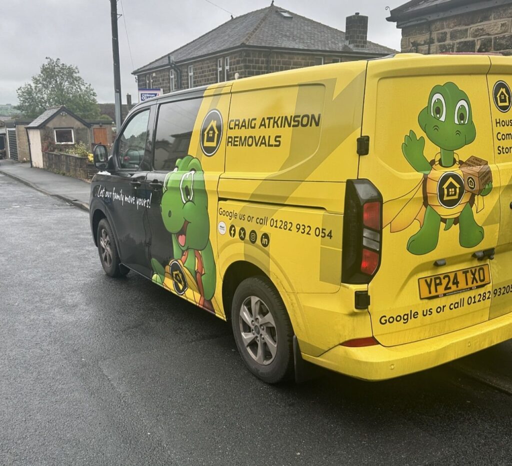 Craig Atkinson Removals small van featuring the company’s mascot and slogan “Let our family move yours” parked on a residential street in Burnley.