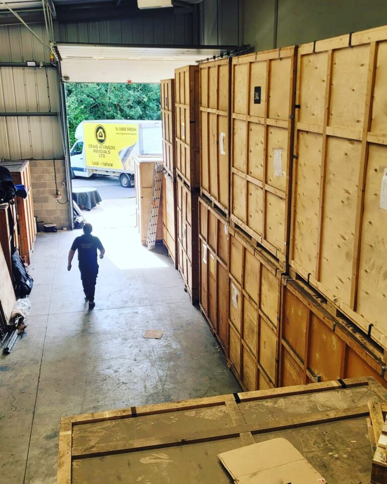Craig Atkinson Removals team member walking through a secure wooden container storage facility with branded van outside.