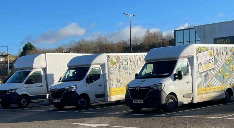 Craig Atkinson Removals vans lined up in Preston, featuring the “Where’s Turbo?” branded design under a clear blue sky.