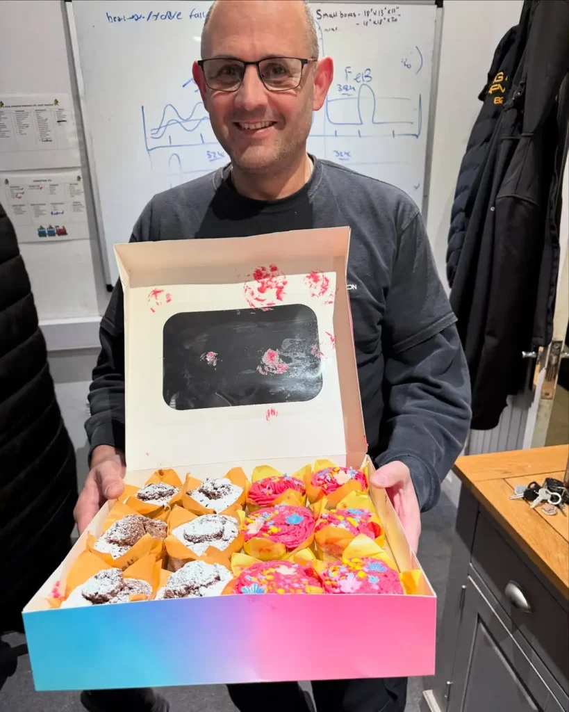 A Craig Atkinson Removals team member holding a colourful box of homemade cupcakes baked by Tobi’s wife.