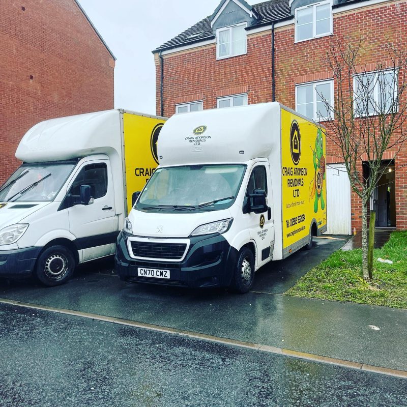 Craig Atkinson Removals vans parked outside a modern red-brick townhouse in Manchester during a local move.